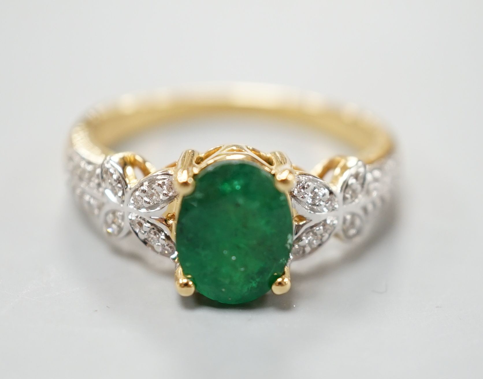 A modern 18ct gold and single stone emerald set dress ring, with diamond chip set shoulders, size R, gross weight 5.5 grams.